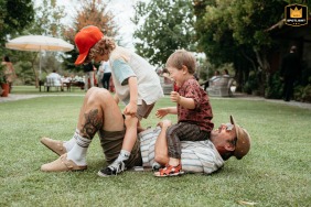 At Quinta da Eira in Penafiel, Portugal, children joyfully jump onto their dad’s belly as he lies on his back in the grass during their aunt’s wedding, capturing playful family interactions in the scenic northern Portuguese countryside.